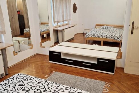Bedroom with a bed in the foreground covered by a white duvet with black heart patterns, plus large wall mirrors and wooden furniture.