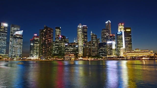 Night view of a modern city skyline along a waterway, with illuminated skyscrapers reflecting on the calm river.